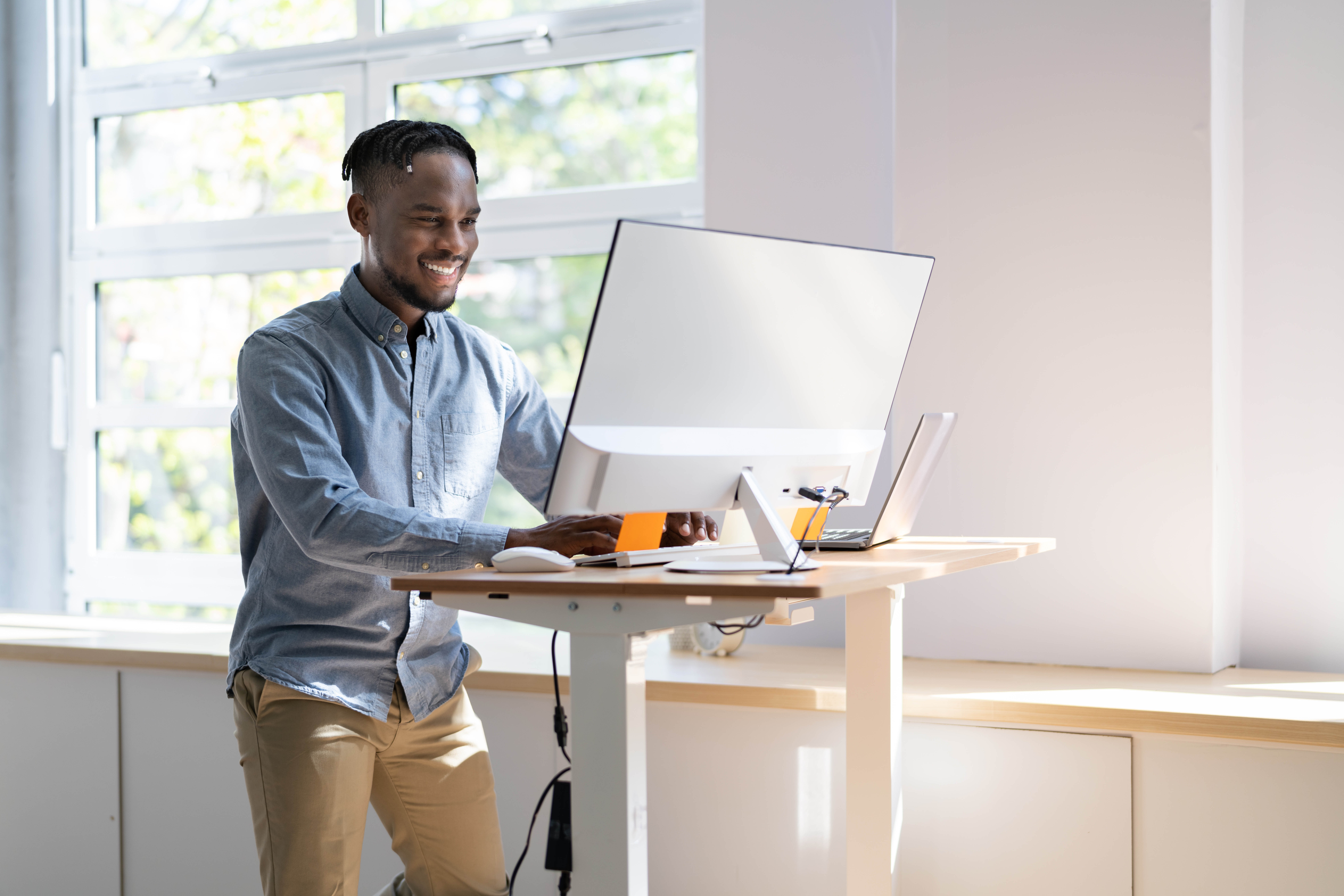 Young, professional black man stands at his standing desk completing work on the screen